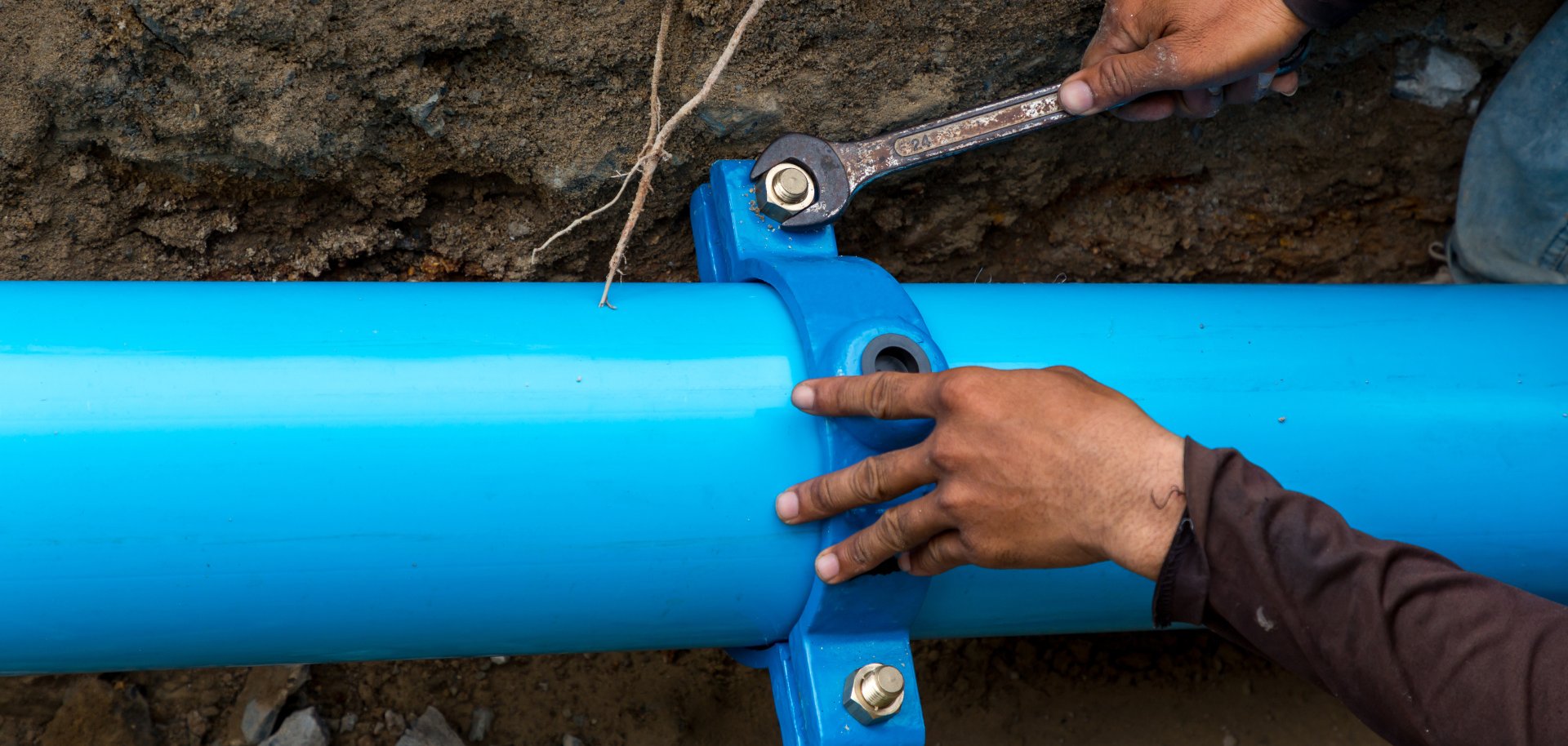 Man using a large wrench on water pipes. Construction site with new Water Pipes in the ground. Sewer pipes to repair or restore in street city.