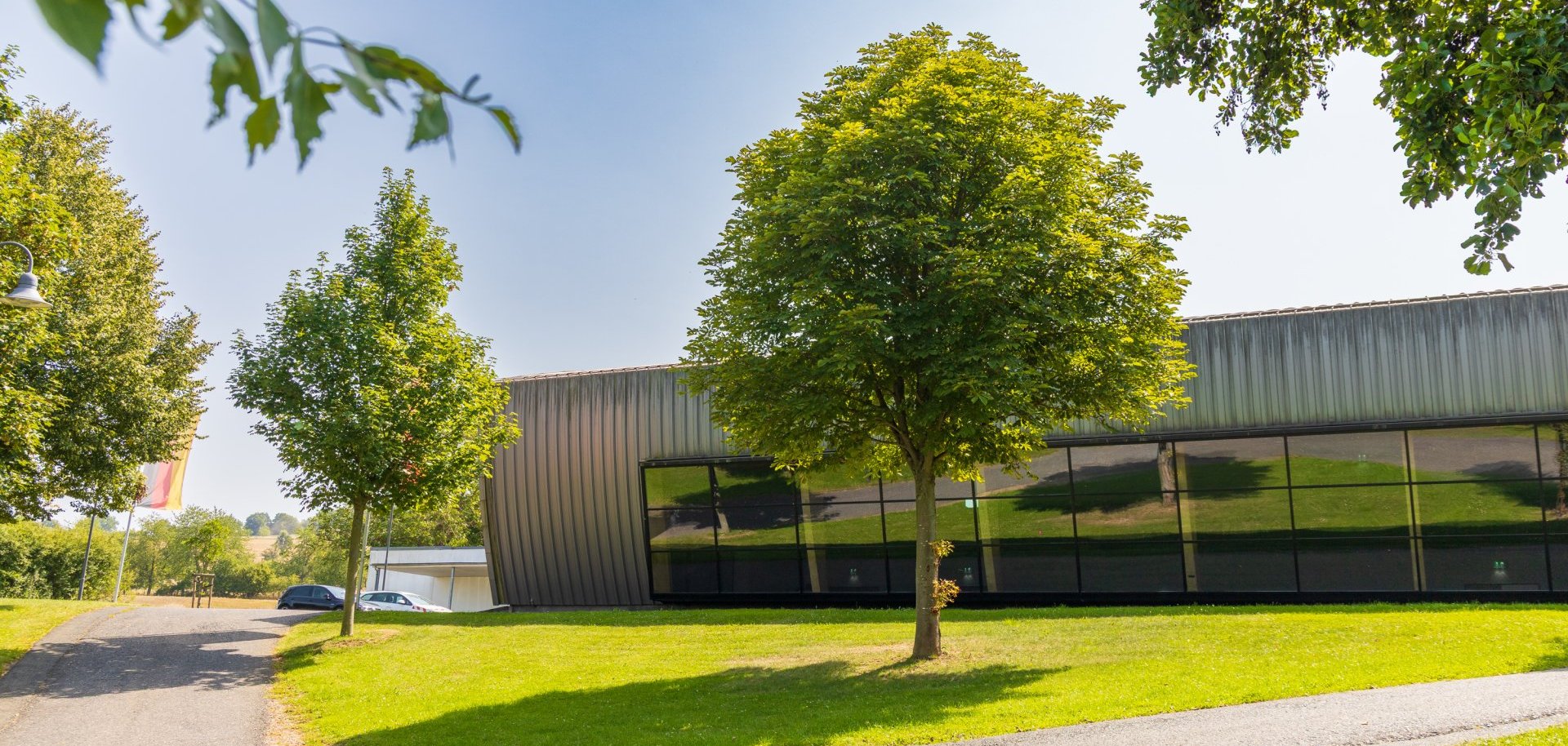 Große moderne Halle mit Glasfront, umgeben von grüner Wiese und Bäumen Große moderne Halle mit Glasfront, umgeben von grüner Wiese und Bäumen