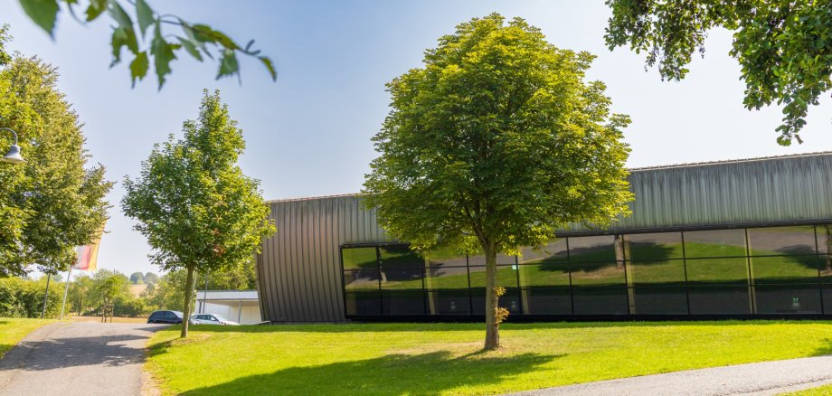 Große moderne Halle mit Glasfront, umgeben von grüner Wiese und Bäumen