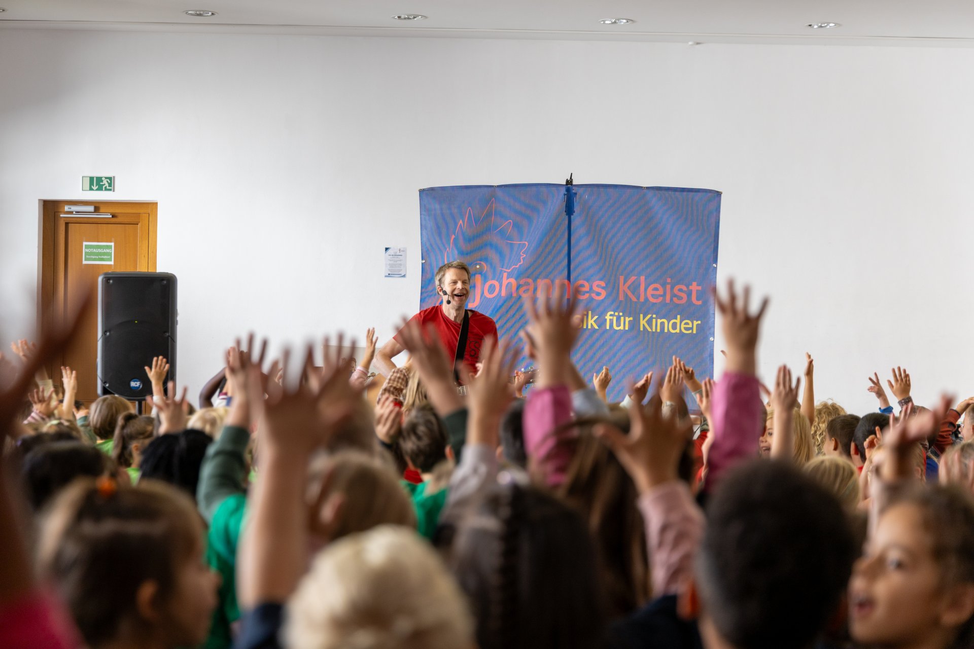 Kinder jubeln mit hochgehaltenen Händen vor einem auf einer Bühne singenden Mann