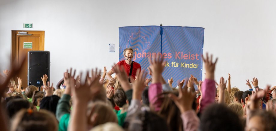 Kinder jubeln mit hochgehaltenen Händen vor einem auf einer Bühne singenden Mann